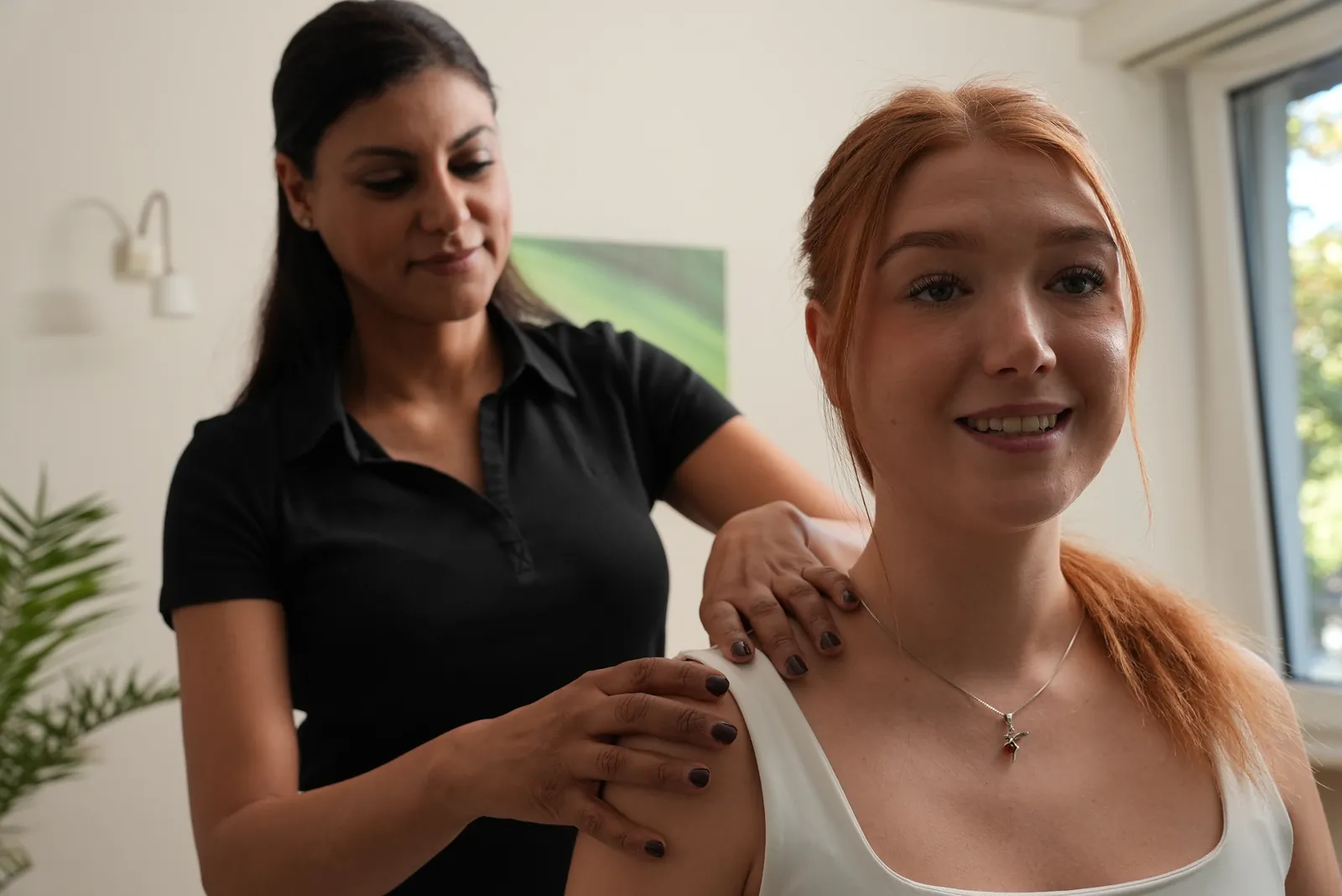 Physiotherapeutin behandelt die Schulter einer lächelnden Patientin mit Manueller Therapie